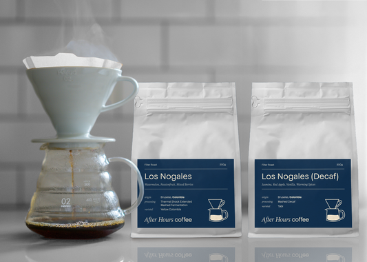 Featured November coffee of Colombian Los Nogales, both decaf and thermal shock processed in 200g retail bags beside a pour over that is being brewed, fresh and crisp.